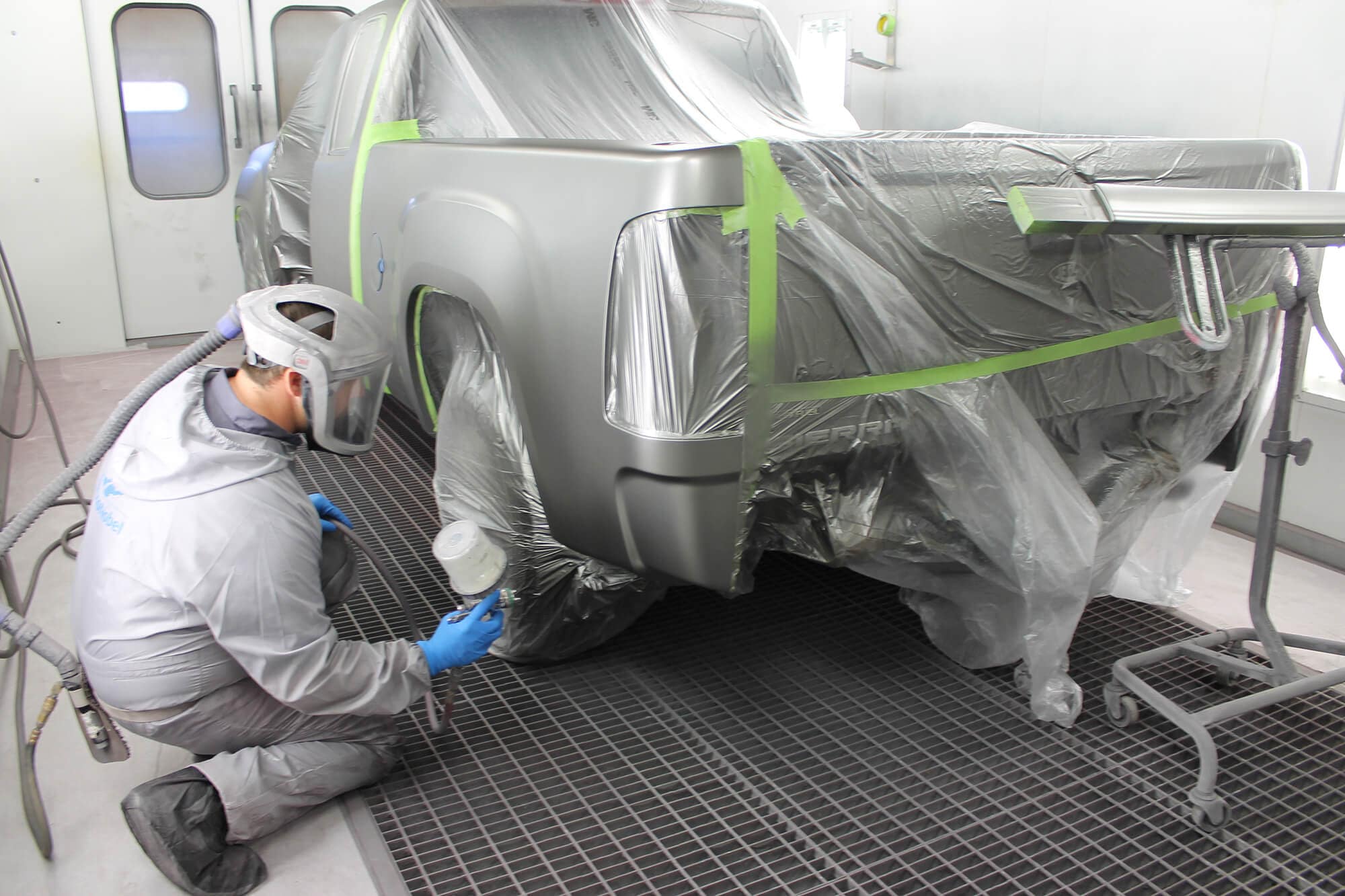 A Rusty Drewing Collision Center refinish technician masking a pickup bed inside the paint booth